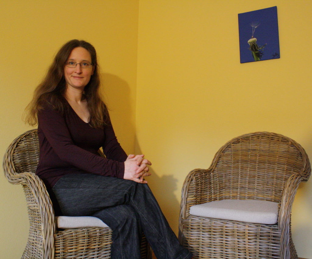 A woman sitting on a wicker chair looking at the camera. Next to her there is another empty wicker chair