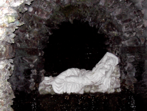 spring equinox: photo of a statue of persephone. she is made from a white stone and reclining in a black grotto